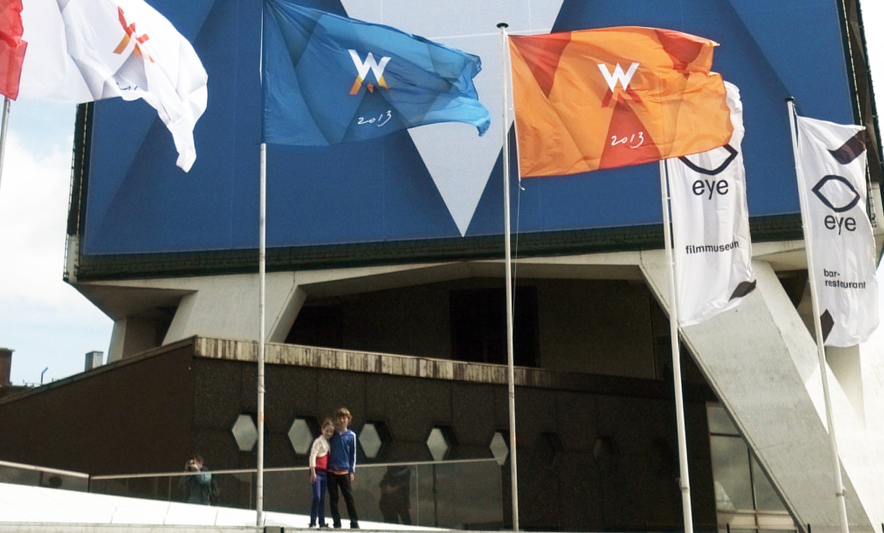 drapeaux aux couleurs déclinées d'une même identité visuelle, devant un bâtiment public